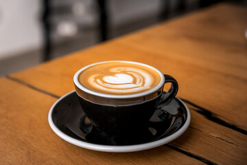 Latte arts coffe. Black cup of hot coffee on wooden table. Cafe with barista art concept.