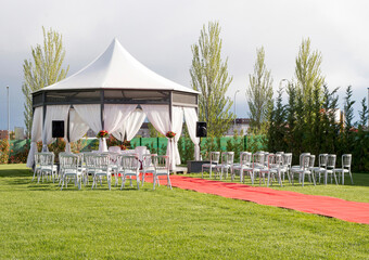 Outdoor chairs placed in the garden next to the red carpet and bridal tent on the wedding day