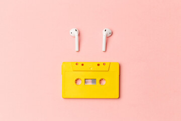 Yellow audio cassette and modern wireless headphones on a pink background. Comparison of old and new technologies. Listening to music, music lovers. Top view. Flat lay - obrazy, fototapety, plakaty