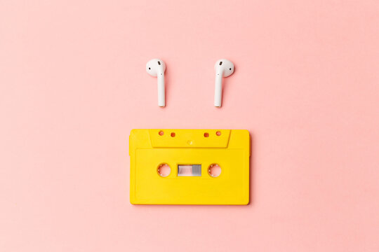 Yellow audio cassette and modern wireless headphones on a pink background. Comparison of old and new technologies. Listening to music, music lovers. Top view. Flat lay