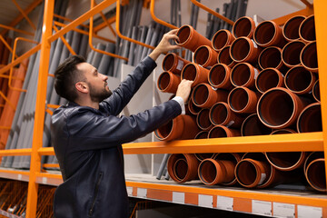male plumber in a hardware store chooses the sewer pipes, the concept of plumbing work in the house