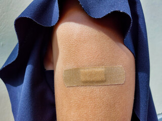 View of a caucasian girl in dark blue blouse with naked upper arm with brown bandaid after getting a dose of the COVID-19 vaccine outdoors in bright sunlight