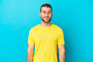 Young handsome caucasian man isolated on blue background making doubts gesture looking side