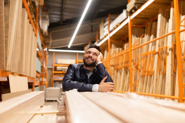 happy customer in a hardware store looks at racks with planks and wooden blocks, with plywood and chipboard and OSB sheets