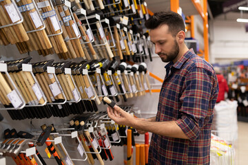 a man in a hardware store picks a hammer next to a display case with hammers and nail pins