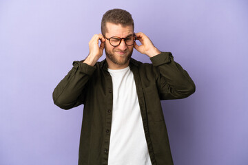 Young handsome caucasian man isolated on purple background frustrated and covering ears