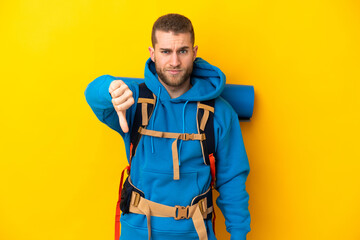 Young caucasian mountaineer man with a big backpack isolated on yellow background showing thumb down with negative expression