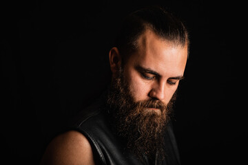 Portrait of a bearded biker man in a black leather vest, looking down in depression and despair