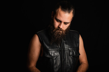 Fototapeta na wymiar Portrait of a bearded biker man in a black leather vest, looking down in depression and despair