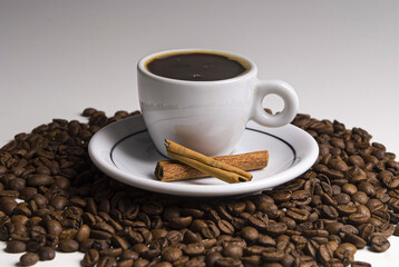 .Cup of coffee served with cinnamon and coffee beans around on black and white background.
