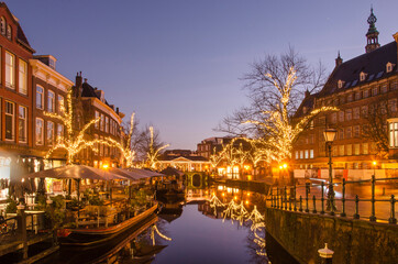 Fototapeta na wymiar Leiden, The Netherlands, December 16, 2021: view along Nieuwe Rijn (New Rhine) canal during the blue hour on a windless winter evening