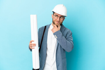 Young architect man with helmet and holding blueprints over isolated background looking to the side...