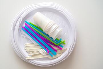 Plates, straws, knives, forks, glasses, disposable plastic objects, photographed closely. Plastic recycling and sales ban.