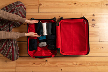 Hands putting clothes in a red suitcase areal view