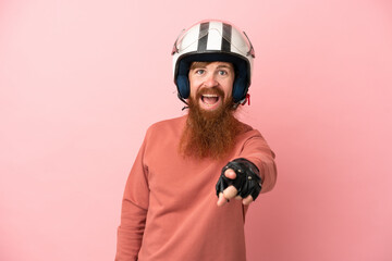 Young reddish caucasian man with a motorcycle helmet isolated on pink background surprised and...