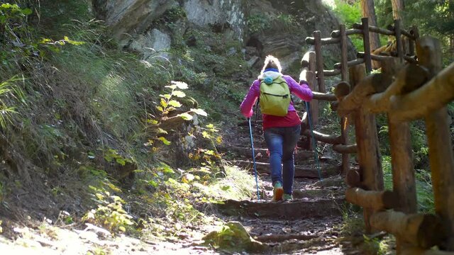 Girl climbs with hiking sticks mountain trail. Slow motion 4K