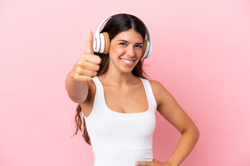 Naklejka premium Young caucasian woman isolated on pink background listening music and with thumb up