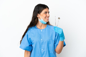 Dentist woman holding tools over isolated white background looking to the side and smiling