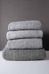 stack of warm grey knit sweaters on white table and gray background. Cold autumn season texture...