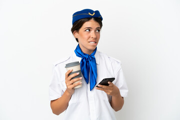 Airplane stewardess caucasian woman isolated on white background holding coffee to take away and a mobile while thinking something