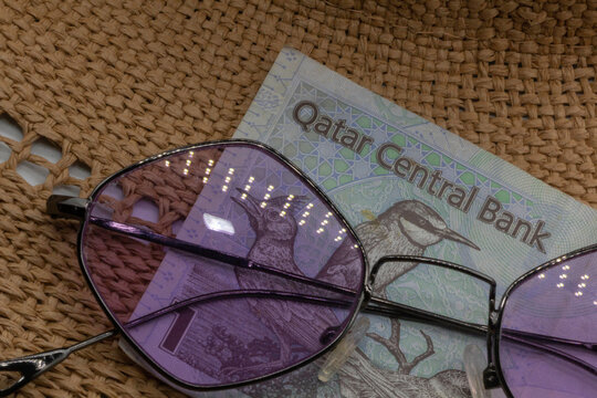 Straw hat, brightly colored glasses and Qatar Rial. Holiday image