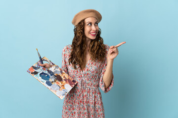 Young artist girl holding a palette isolated on blue background intending to realizes the solution...