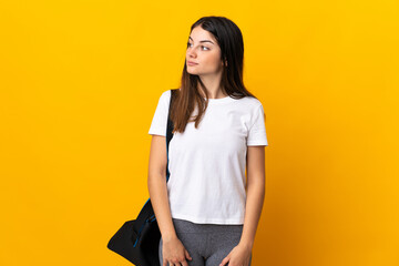 Young sport woman with sport bag isolated on yellow background looking to the side