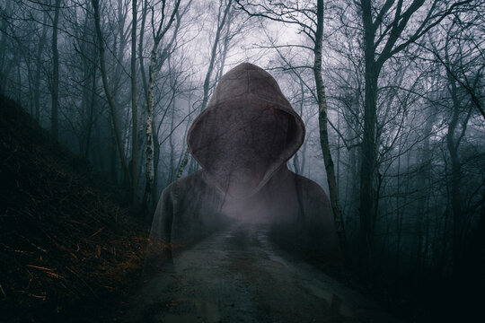 A horror concept of a double exposure of a scary hooded figure with no face. In a moody, foggy forest on a winters evening