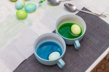 Easter eggs are painted in green and blue colors in plates with water with dye before Easter