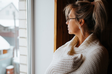 Side view portrait of sad lonely adult caucasian woman wrapped in warm cozy knitted blanket...