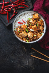 Bowl of chinese mapo tofu with rice over dark-brown stone background, vertical shot with space, view from above