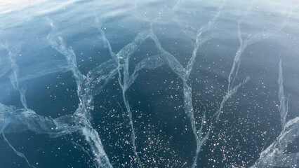 Transparent blue ice of Lake Baikal. Close-up. Full screen. Top view. Deep intersecting cracks are visible, snowflakes on the surface.