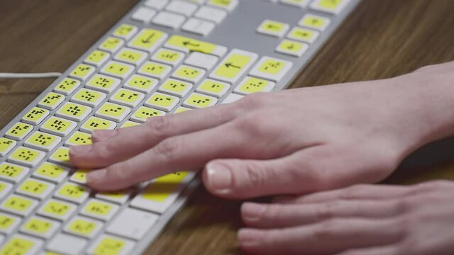Close-up of a computer keyboard with braille. A blind girl is typing words on the buttons with her hands. Technological device for visually impaired people. Tactilely touches bumps on the keys