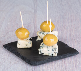 Canapes of blue cheese and large green olives on a black slate cutting board