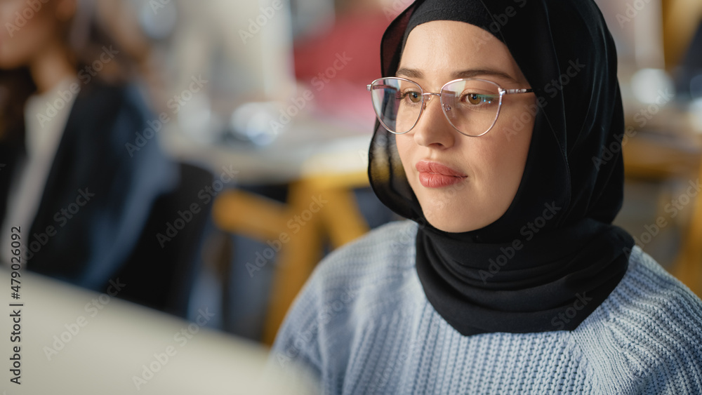 Poster beautiful portrait of a female muslim student in hijab, studying in university. she works on desktop