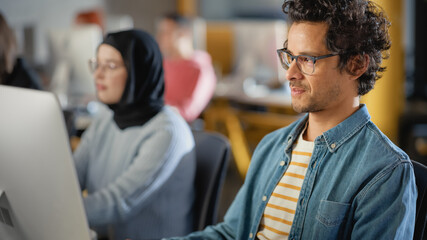 Portrait of a Handsome Smart Male Student in Glasses, Studying in Modern University with Diverse Multiethnic Classmates. Works on Computer in College. Applying His Knowledge and Skills.