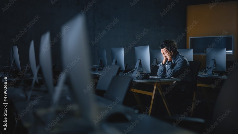 Fototapete Stressed Male Student Sitting Alone in College Informatics Room, Working Late Evenings on Computer Science Project. Tired Scholar Study IT on Computer in University, Writing Homework.