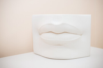 Lips plaster casting in a sculpting studio used for clay modelling workshops by sculptors.White plaster lips on pastel background. cosmetologist,permanent makeup, lip augmentation
