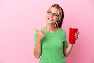 Young Russian woman holding a refreshment isolated on pink background pointing to the side to present a product