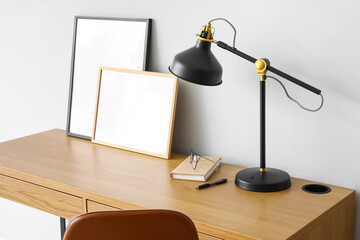 Modern workplace with black lamp and frames near light wall