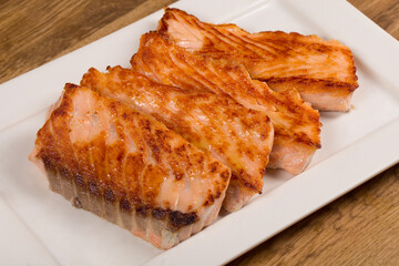Grilled salmon fillet served on white plate on wooden background.