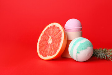 Composition with bath bombs, grapefruit and fir branch on red background