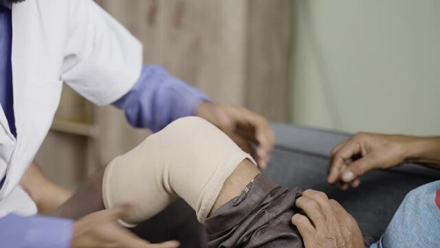 Close up shot of unrecognizable Physician treating old man by wearing stretch bandage for knee sprain or joint paint- concept of senior people muscle injury, healthcare treatment.