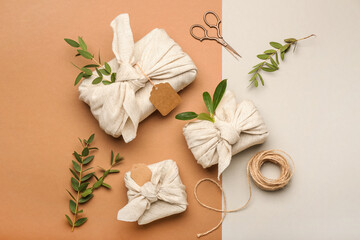 Gift boxes wrapped in fabric, rope and scissors on color background
