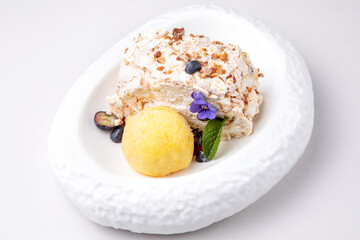 meringue dessert with a scoop of ice cream, decorated with violet and mint leaf