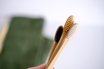 Three bamboo toothbrushes on a green towel with a plant on the background