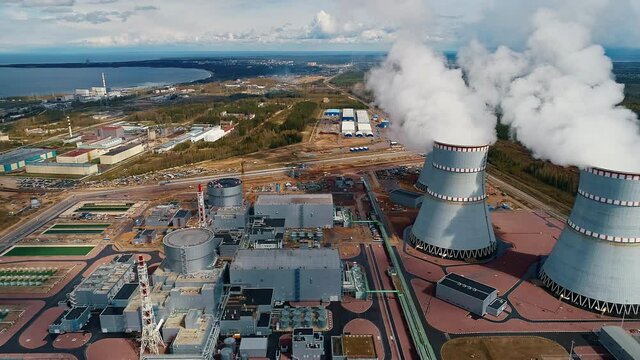 The flight of a drone over power units and cooling towers with steam and smoke from a nuclear power plant on a clear sunny day.