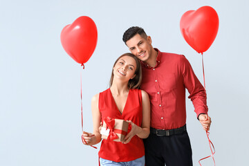 Happy young couple with gift and balloons on grey background. Valentine's Day celebration