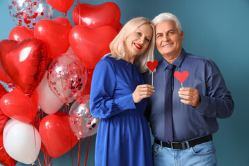 Happy mature couple with party decor and balloons on color background. Valentine's Day celebration