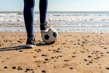 Legs of a girl stepping on a soccer ball on the beach with the sea in the background, she watches...